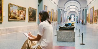 Mujer sentada en un banco dibujando dentro del Museo del Prado