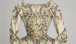 Vista trasera de una casa femenina, s. XVIII, seda labrada, con aplicación de bordado que dibuja motivos florales polícromos.
